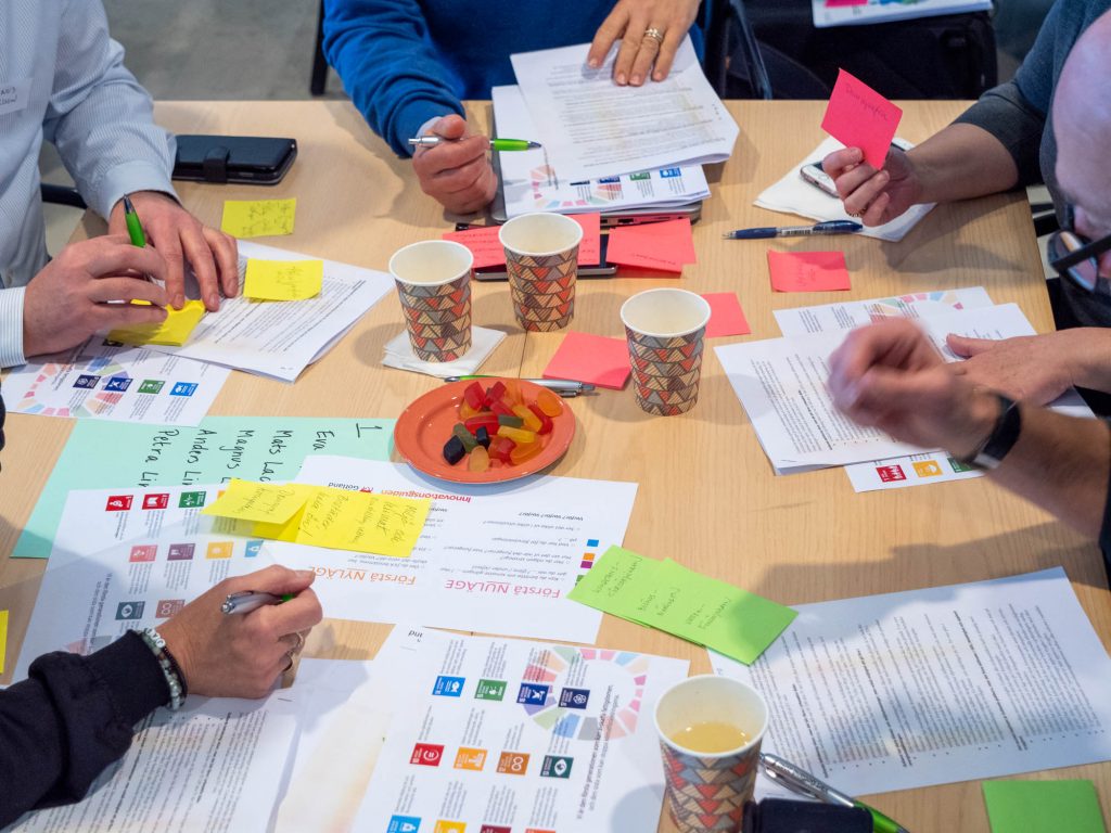 Personer runt ett bord med papper, post-its, kaffemuggar och godis.